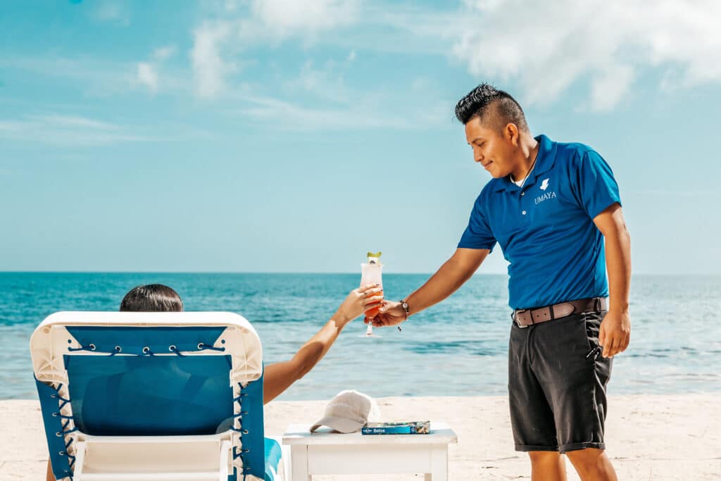 A guest being handed a cocktail by a bartender on the beach at Umaya Resort