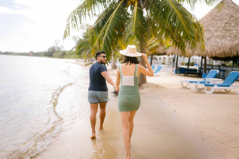 Romantic couple holding hands strolling along the Caribbean beachfront at Umaya Resort, Maya Beach, Placencia Peninsula, Stann Creek District, Southern Belize